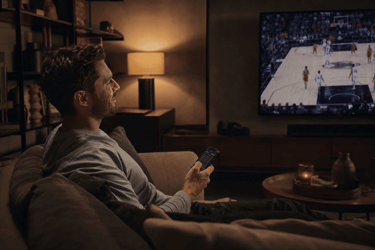 Bettor relaxing on the couch watching basketball with a sports app on phone